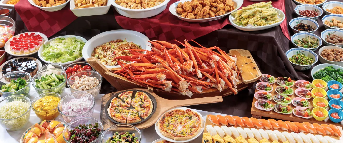 提供される豪華なバイキング料理。舟盛りになった茹でたカニの脚を中心に、手前に寿司、ピザ、左右にサラダバーの具材や小鉢、デザートが並んでいる食欲をそそる一枚。