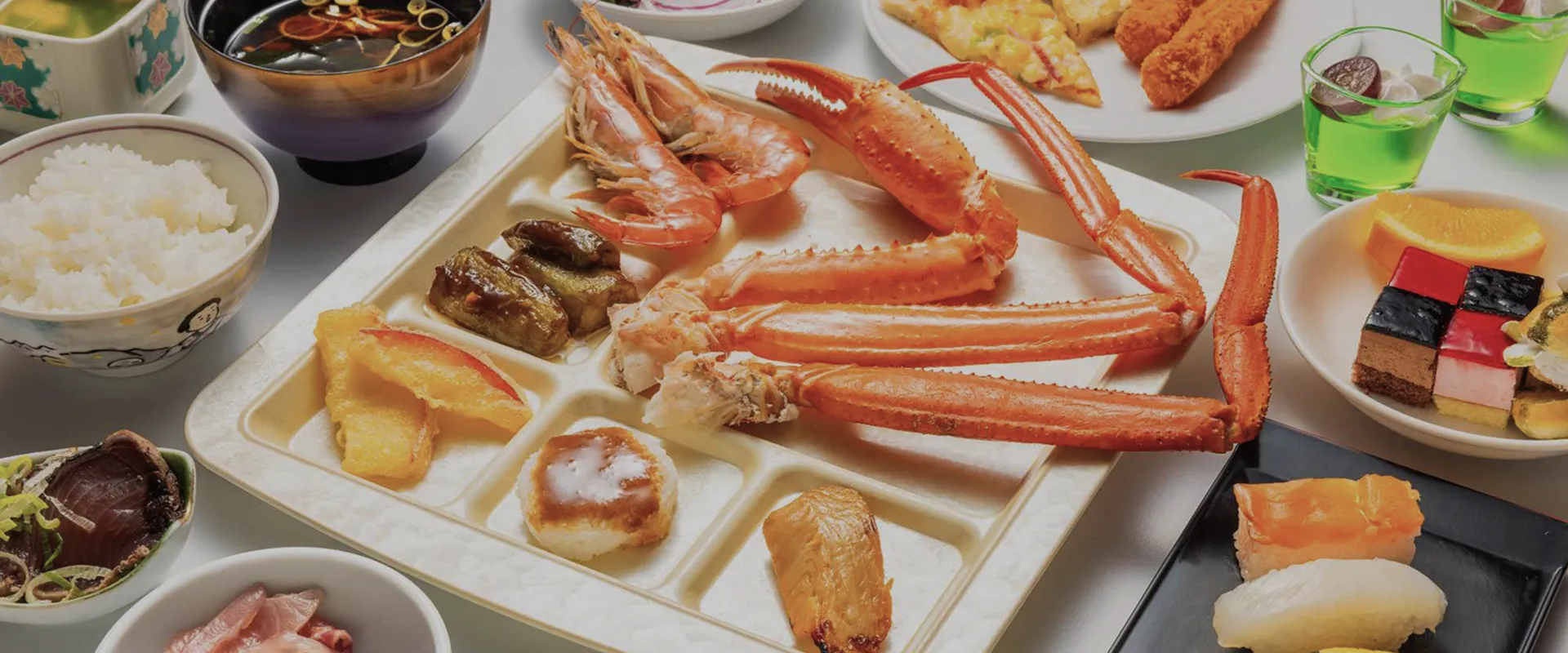 イメージ：メインにカニの足とエビを盛り付けた、和洋折衷のブッフェ料理の写真。ご飯や寿司、デザートも見える