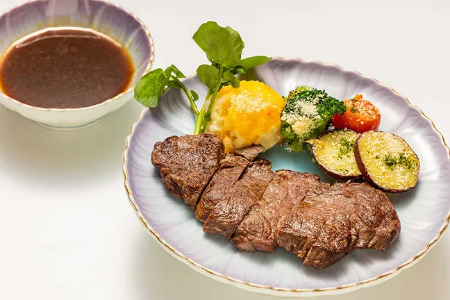 カットされて盛り付けられたミディアムレアの牛ヒレステーキと、添えられた野菜、別添えのソース。