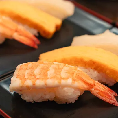 つややかなエビの握り寿司が手前にあり、奥には卵焼き（玉子）の握り寿司が並ぶ、お寿司の盛り合わせのクローズアップ写真。