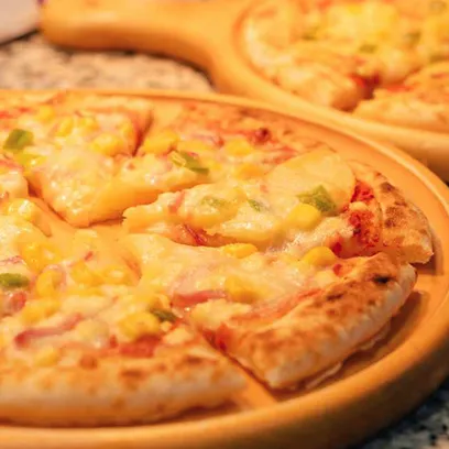 コーンやピーマン、チーズがたっぷり乗ったピザが木製のトレイに置かれ、数切れにカットされているクローズアップ写真。