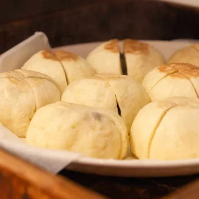 竹製のせいろに、長野県名物のおやきが八つ並んでいるクローズアップ写真。蒸気で温められ、表面に十字の切れ目と味噌餡のような具材が見える。