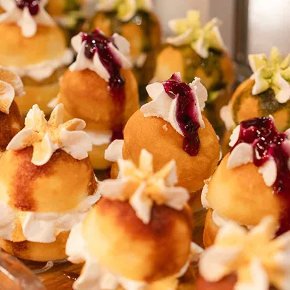 生クリームの上にブルーベリーソースやキャラメルソースがかけられた、ひとくちサイズの丸い揚げドーナツが多数並ぶデザートの写真。