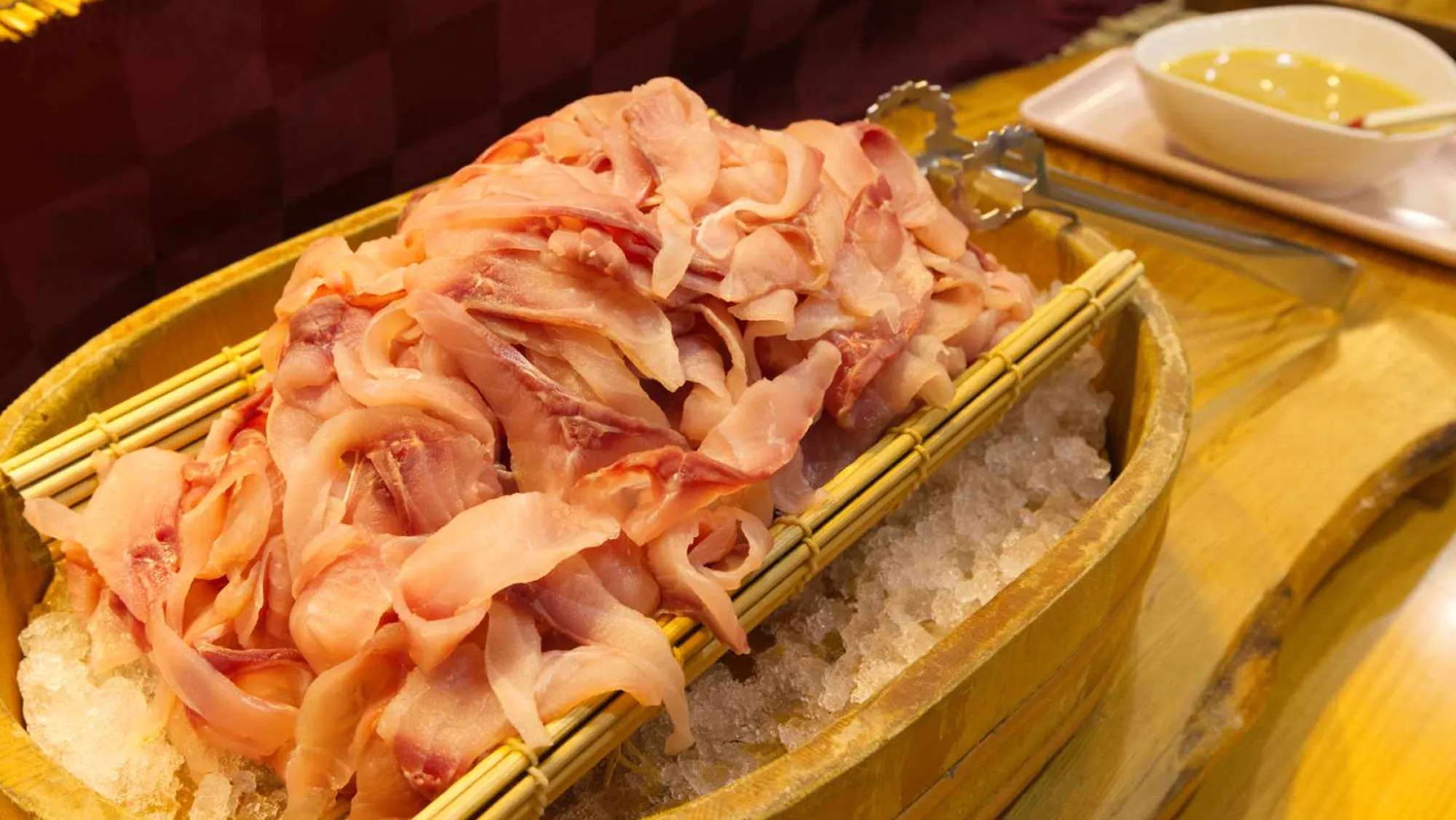 氷を敷き詰めた木製の舟盛り容器に、薄くスライスされた淡いピンク色の魚の刺身が山盛りに盛られている。