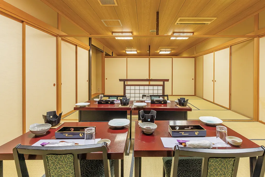 畳敷きの和室に、赤い座卓が二つ向かい合わせに配置され、すでに料理がセットされており、背後に障子と襖に囲まれた落ち着いた設えの中、少人数での会食や家族の集まりに最適な小宴会場の風景である。