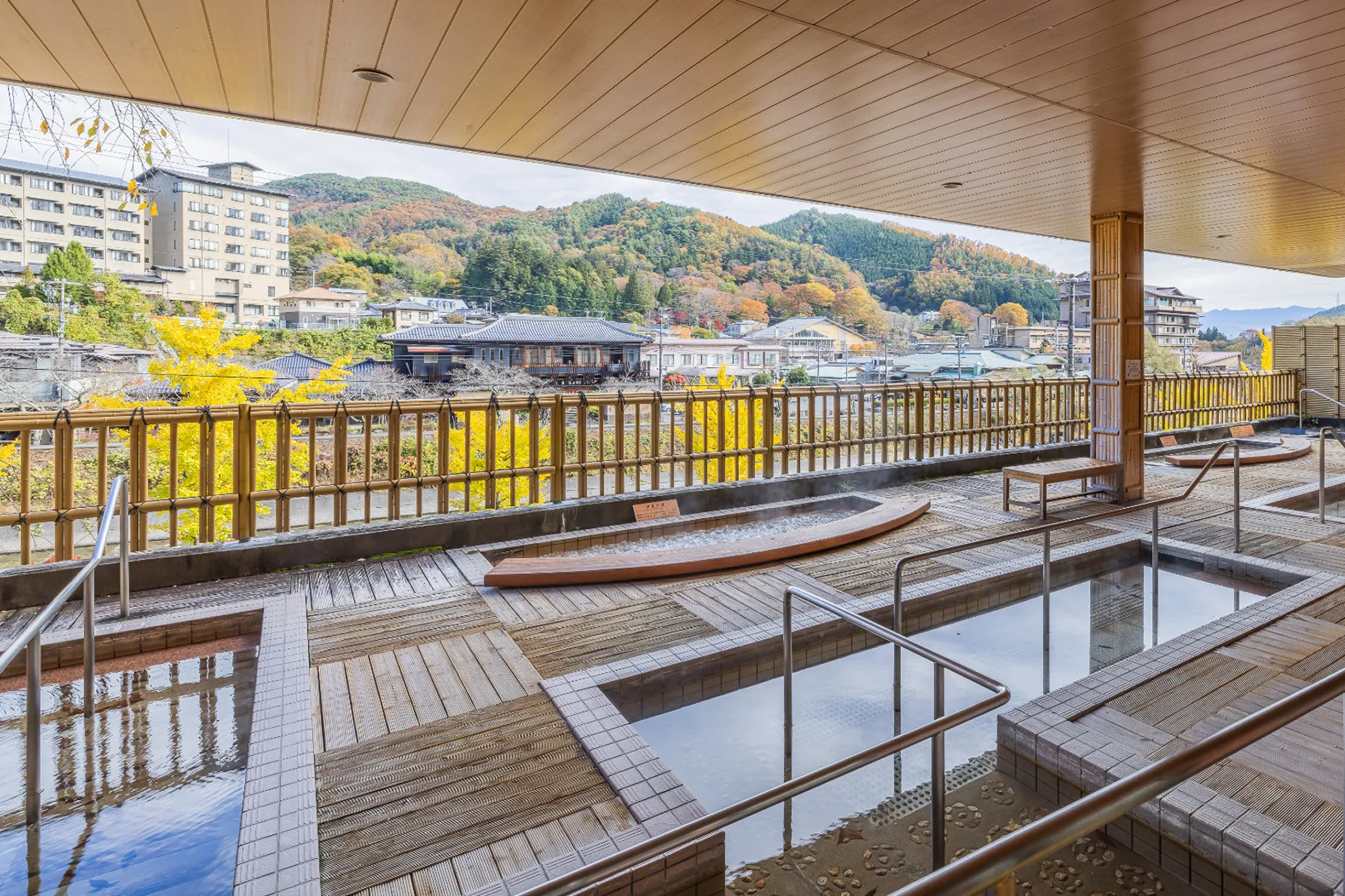 屋根付きの屋外テラスにある足湯スペース。デッキ材の床に、深さの異なる複数の長方形の足湯槽があり、手すりがついている。