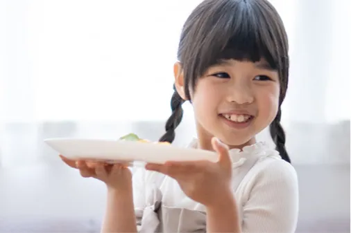 バイキングで選んだお料理のお皿を大切そうに両手で持ち、満面の笑みを浮かべる女の子。