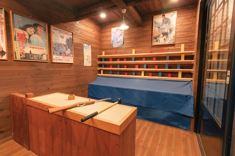 木造りの温かみがある射的コーナー。カウンターにはコルク銃が置かれ、壁には昭和レトロな映画ポスターが飾られた懐かしい雰囲気の遊び場。