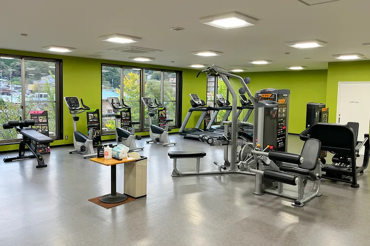 大きな窓から外の景色を眺められる、広々としたフィットネスジム。ランニングマシンやエアロバイク、筋力トレーニング用の本格的なマシンが並ぶ清潔なワークアウトスペース。