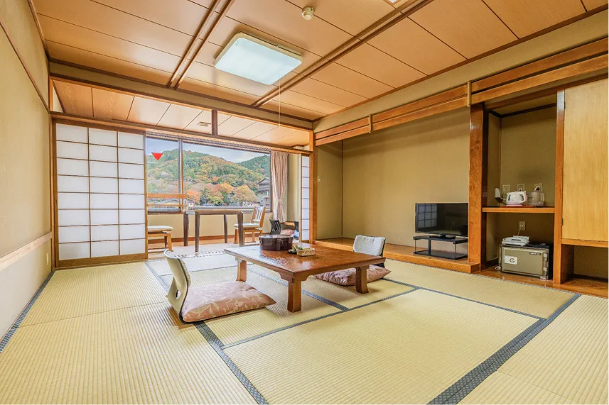 畳の香りが漂いそうな、広々とした和室。中央には座卓と座椅子があり、大きな窓の向こうには紅葉した山々の絶景が広がる、明るく落ち着いた客室。