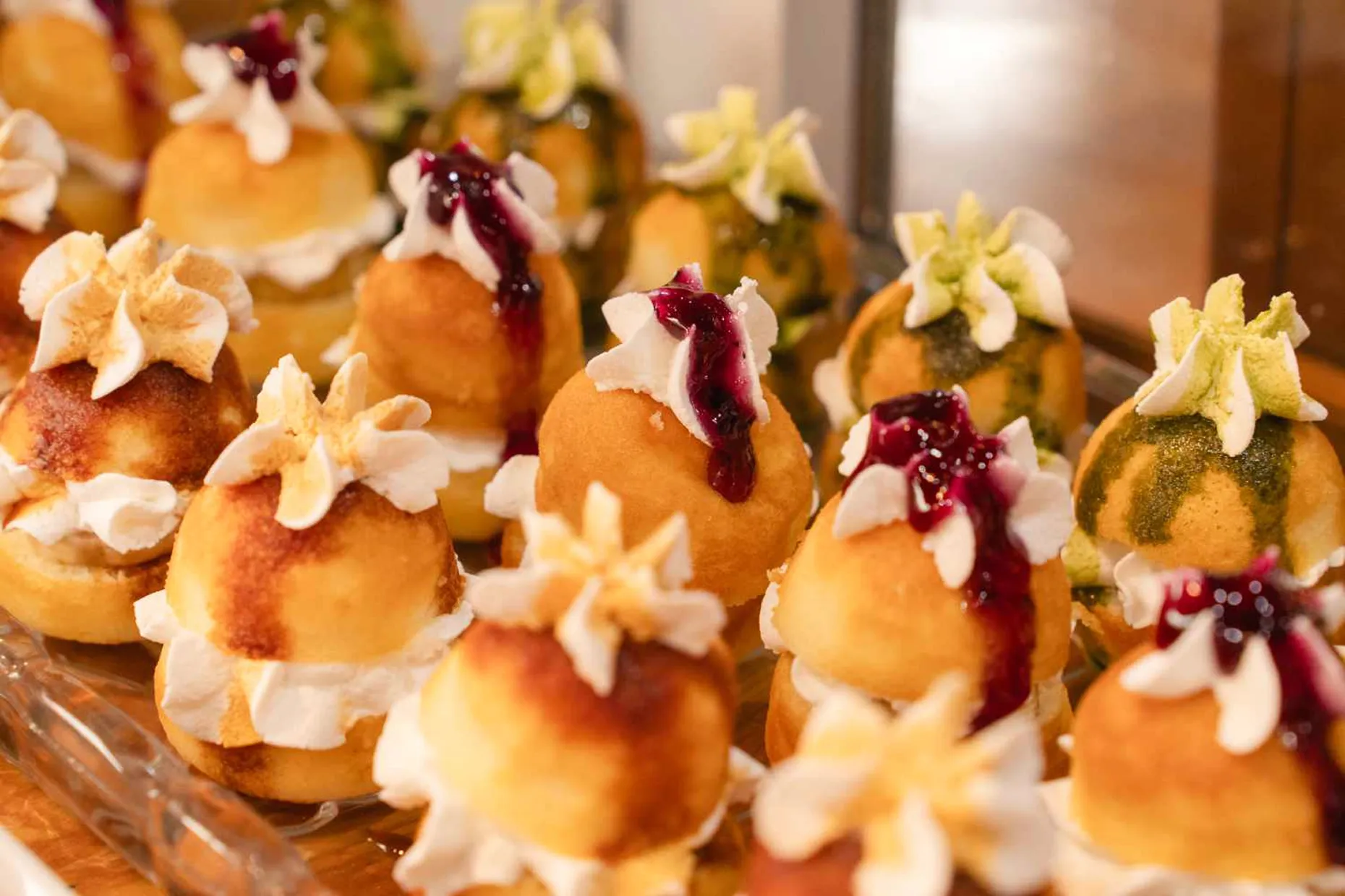 生クリームの上にブルーベリーソースやキャラメルソースがかけられた、ひとくちサイズの丸い揚げドーナツが多数並ぶデザートの写真。