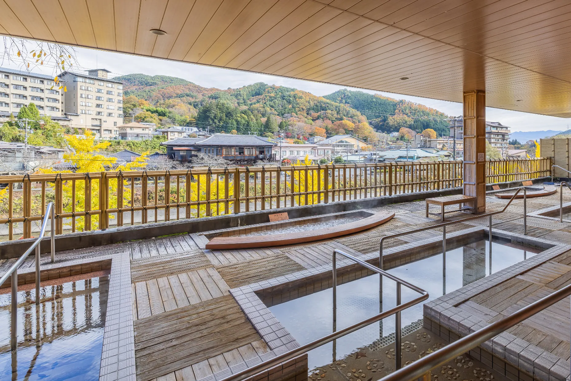 屋根付きの屋外テラスにある足湯スペース。デッキ材の床に、深さの異なる複数の長方形の足湯槽があり、手すりがついている。