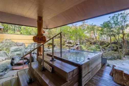 屋根付きの木製デッキと岩に囲まれた、開放的な露天風呂。