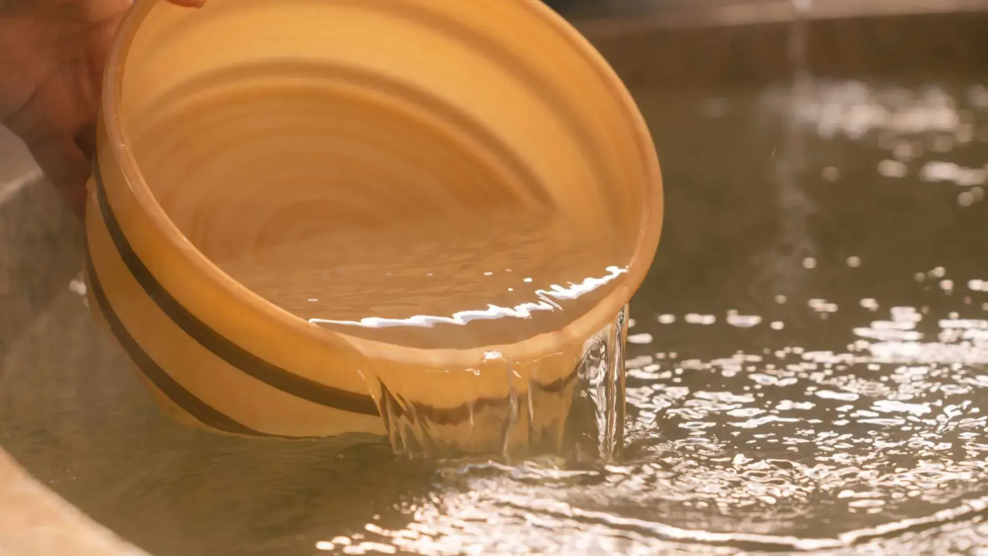 温泉の湯を木製の桶で汲む様子