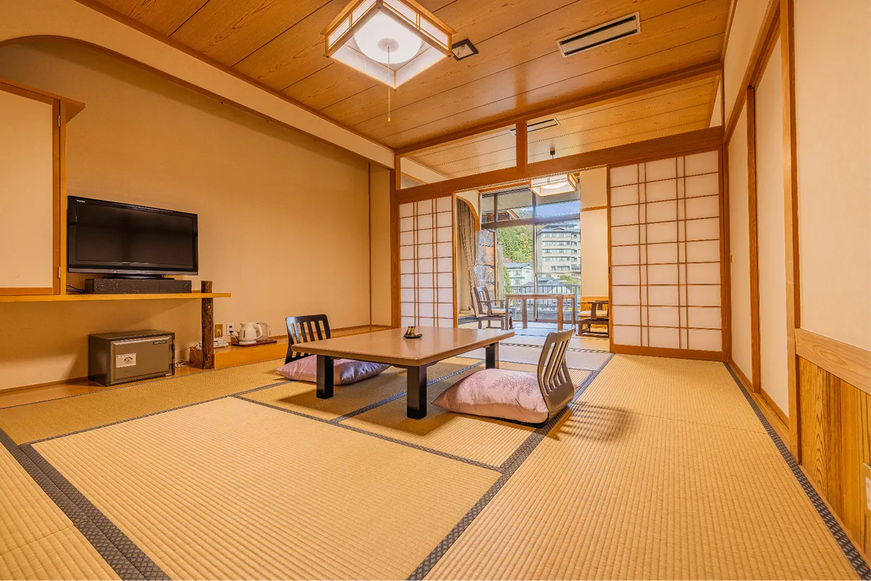 和の情緒あふれる、い草が香る畳敷きの客室。中央には座卓と座椅子が置かれ、奥の障子を開けると、川を望む開放的なテラスへと続いています。