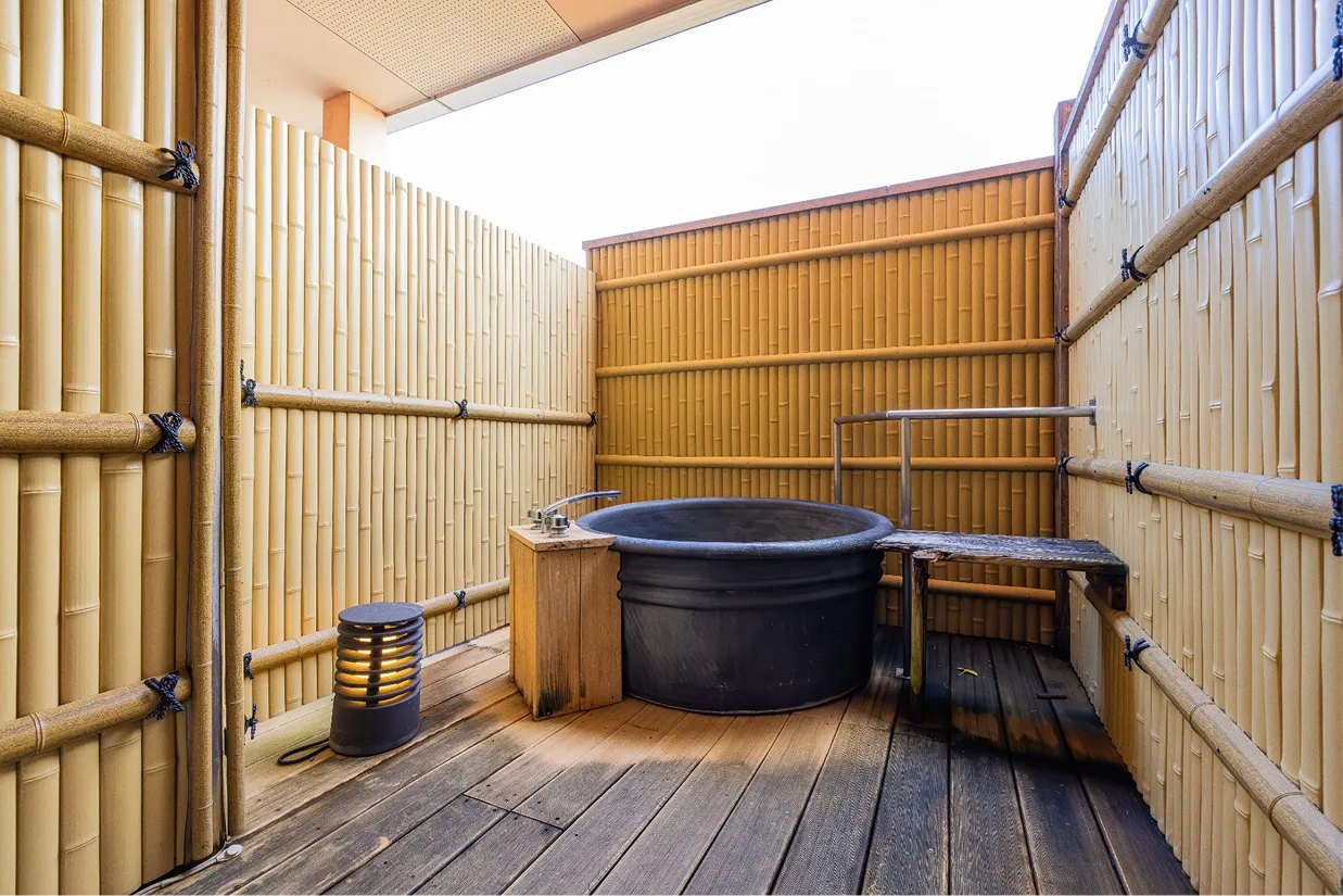 バルコニーのウッドデッキに設置された、風情ある陶器製の丸い露天風呂。周囲は竹垣のパーテーションで囲まれ、プライベートな空間で落ち着いたひとときを過ごせます。