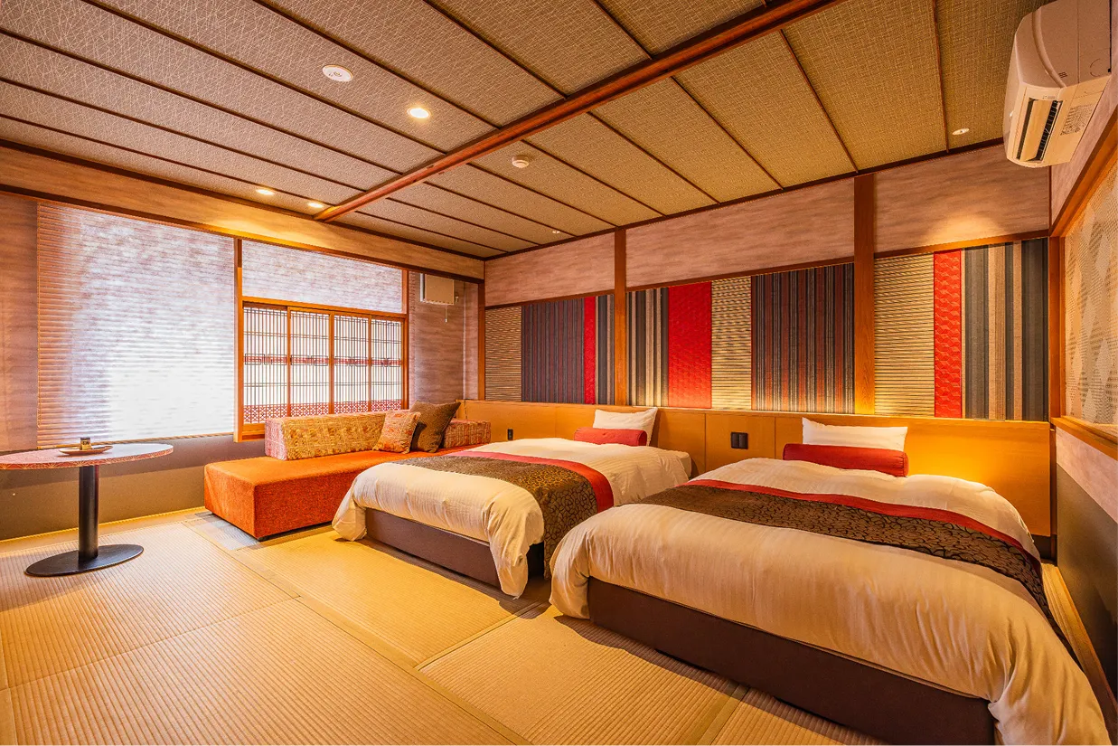 畳敷きの床にベッドが2台並んだバリアフリー洋室。窓側には3名利用時にベッドとなるオレンジ色の大きなソファとテーブルがあり、車椅子でも移動しやすい広々とした空間。
