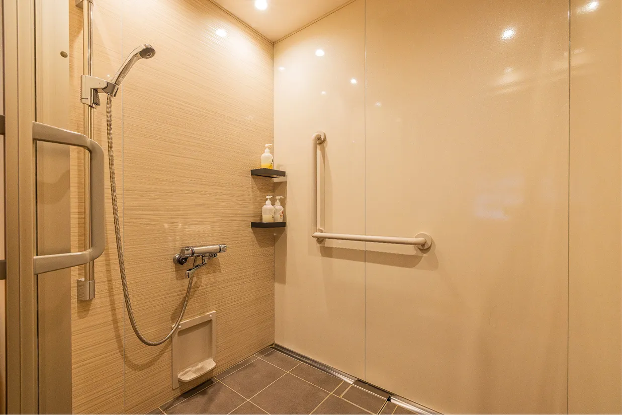段差のないシャワールーム。壁面にはL字型の大きな手すりが設置されており、滑りにくい床材とあわせて、足腰が不安な方でも安心して利用できる設計になっています。