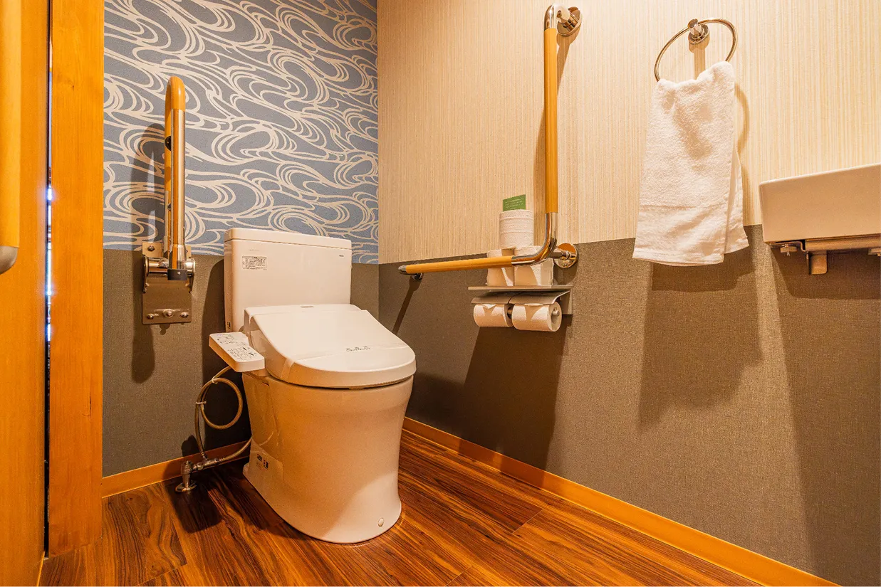 広々としたバリアフリー設計のトイレ。便器の両側には、跳ね上げ式とL字型のしっかりとした手すりが備え付けられており、車椅子からの移乗もしやすいゆとりあるスペースです。