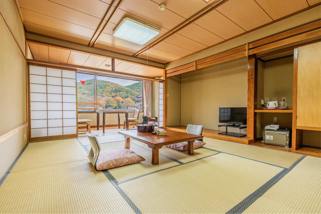 畳の香りが漂うような10畳の和室。中央には座椅子を備えた長方形の座卓があり、奥の広縁からは色づく山々の景色を眺めることができます。