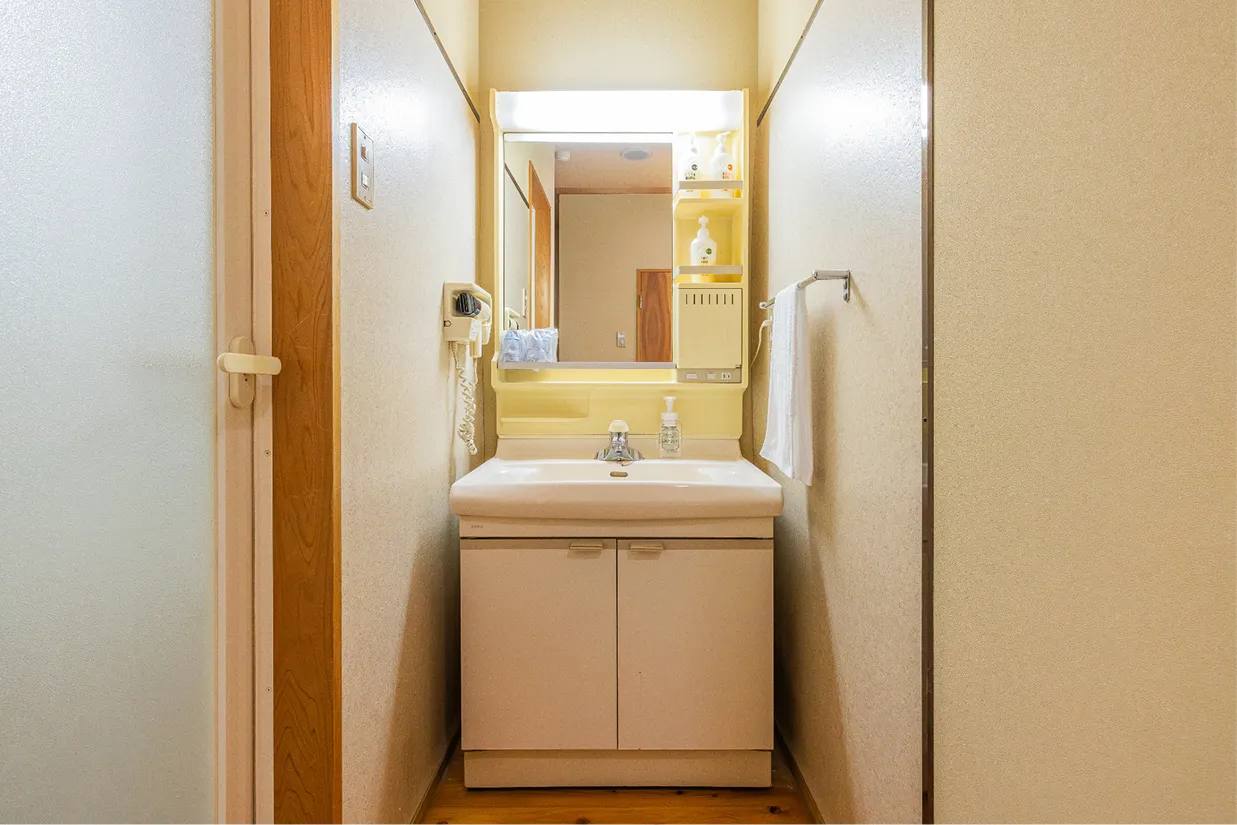 機能的な独立洗面台。大きな鏡の横にはアメニティ類が整えられており、壁面にはドライヤーとタオル掛けが備わっています。明るく使い勝手の良い空間です。